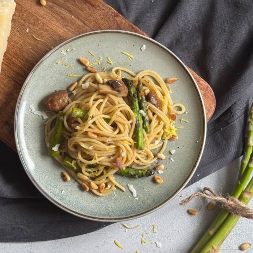 Ein Teller mit Pasta, gruenem Spargel, mit gehobeltem Parmesan und Pinienkernen