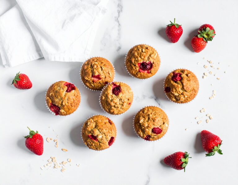 Acht goldbraune Erdbeermuffins von oben auf Marmor, garniert mit frischen Erdbeeren und Haferflocken